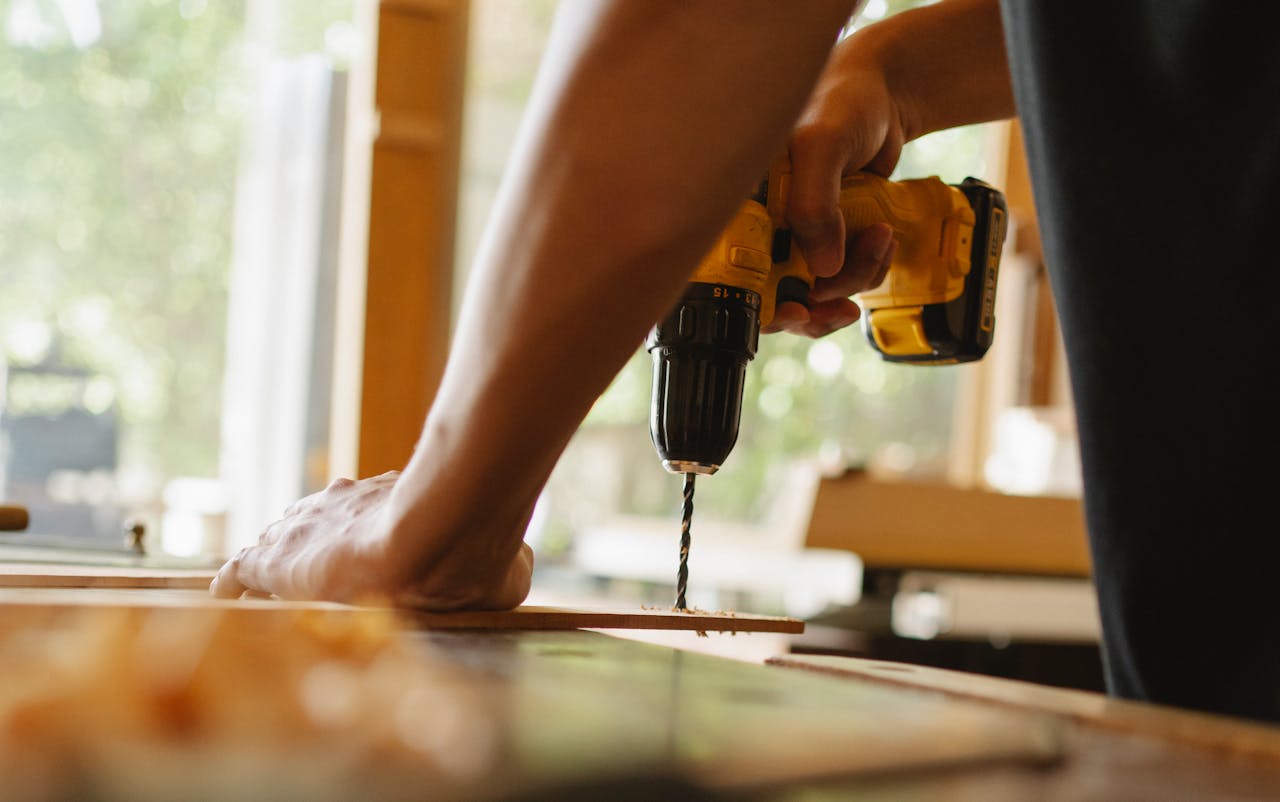 about-us-02 Close-up of a person using a power drill on wood indoors during daytime.